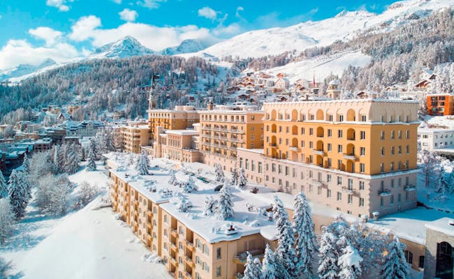 Kulmhotel i St. Moritz, omgiven av snötäckta berg och färgglada hus.