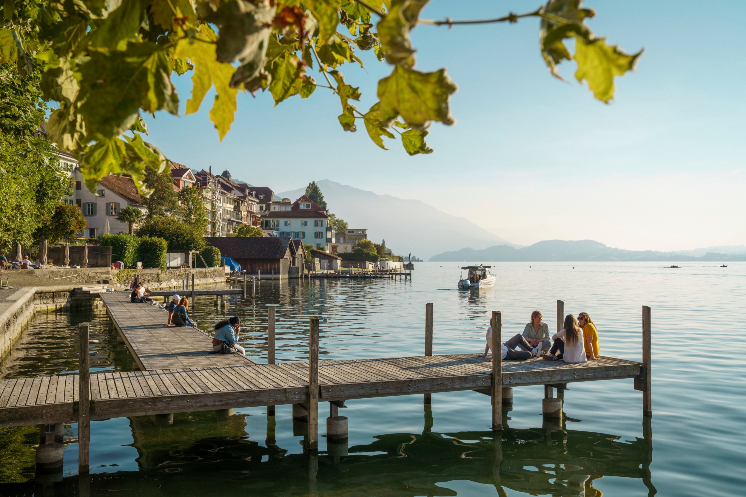 Lago di Zugo con una barca e passeggiatori sul molo