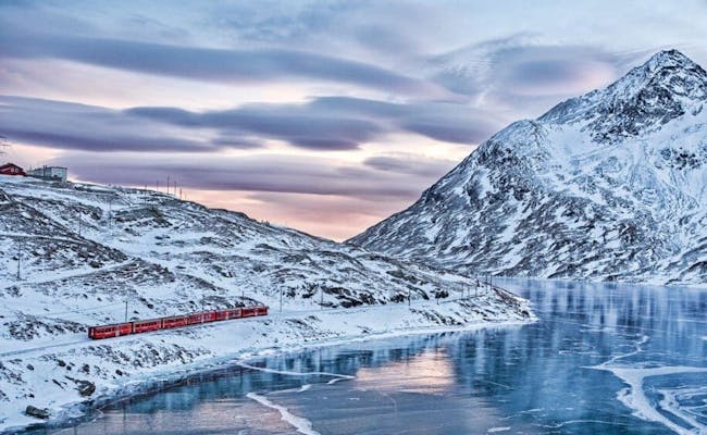รถไฟ Bernina Express ขับผ่านภูมิทัศน์ที่ปกคลุมไปด้วยหิมะเคียงข้างทะเลสาบที่กลายเป็นน้ำแข็ง.