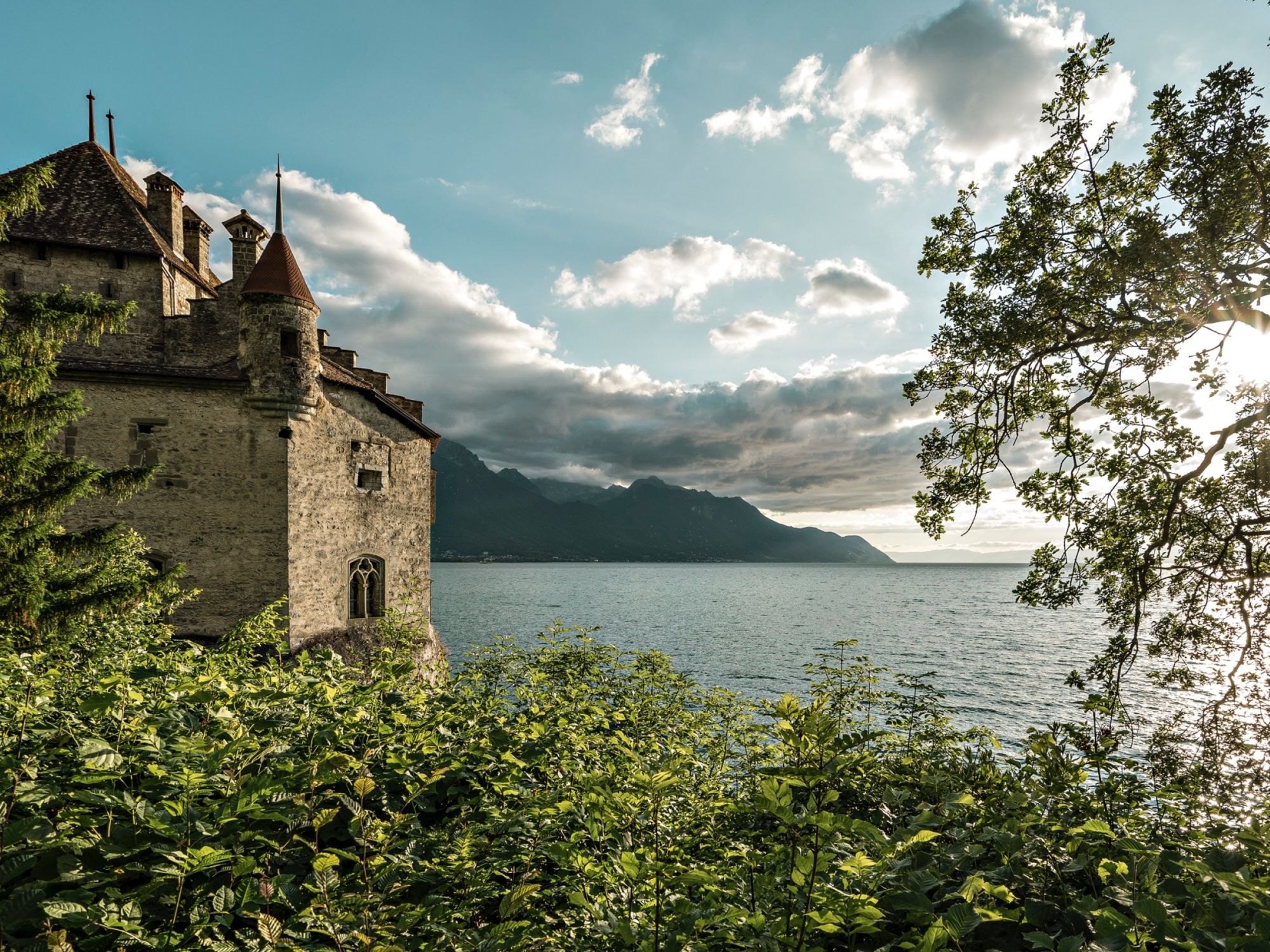Chateau Chillon på våren vid Genèvesjön med träd och berg i bakgrunden.