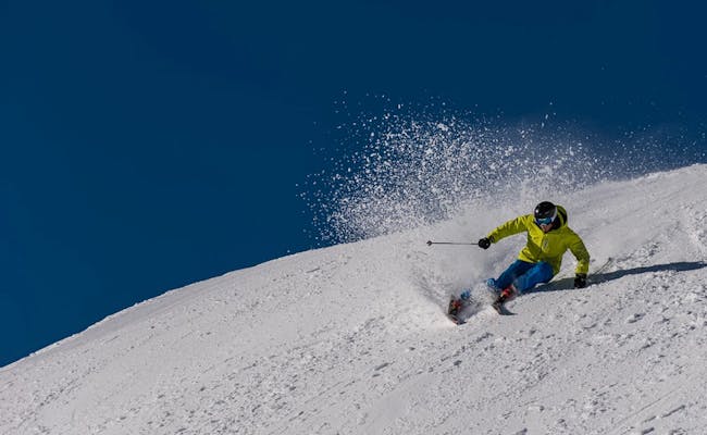 Skifahren auf der Tschentenalp mit blauer Himmel, Schnee und Skifahrer in grüner Jacke.