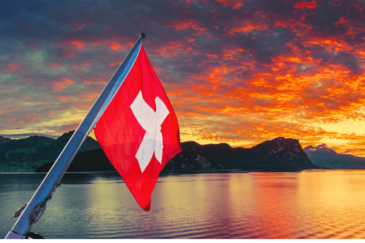 यॉट नाइट इवेंट: झरने पर सूर्यास्त, पर्वतीय परिदृश्य और स्विट्जरलैंड ध्वज के साथ।