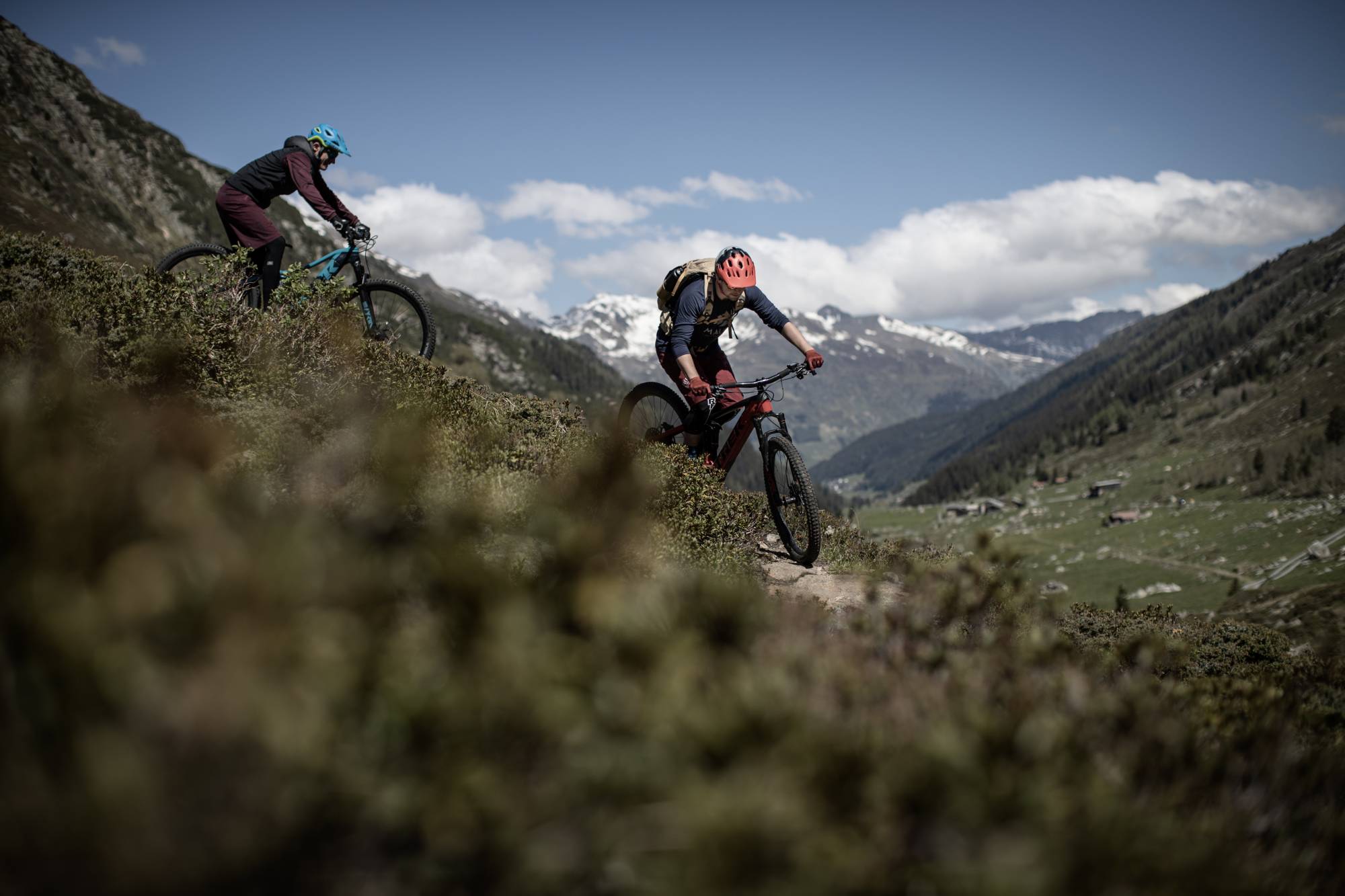 Bike Tour Davos: Two mountain bikers ascend a steep path in the Alps on a clear day.