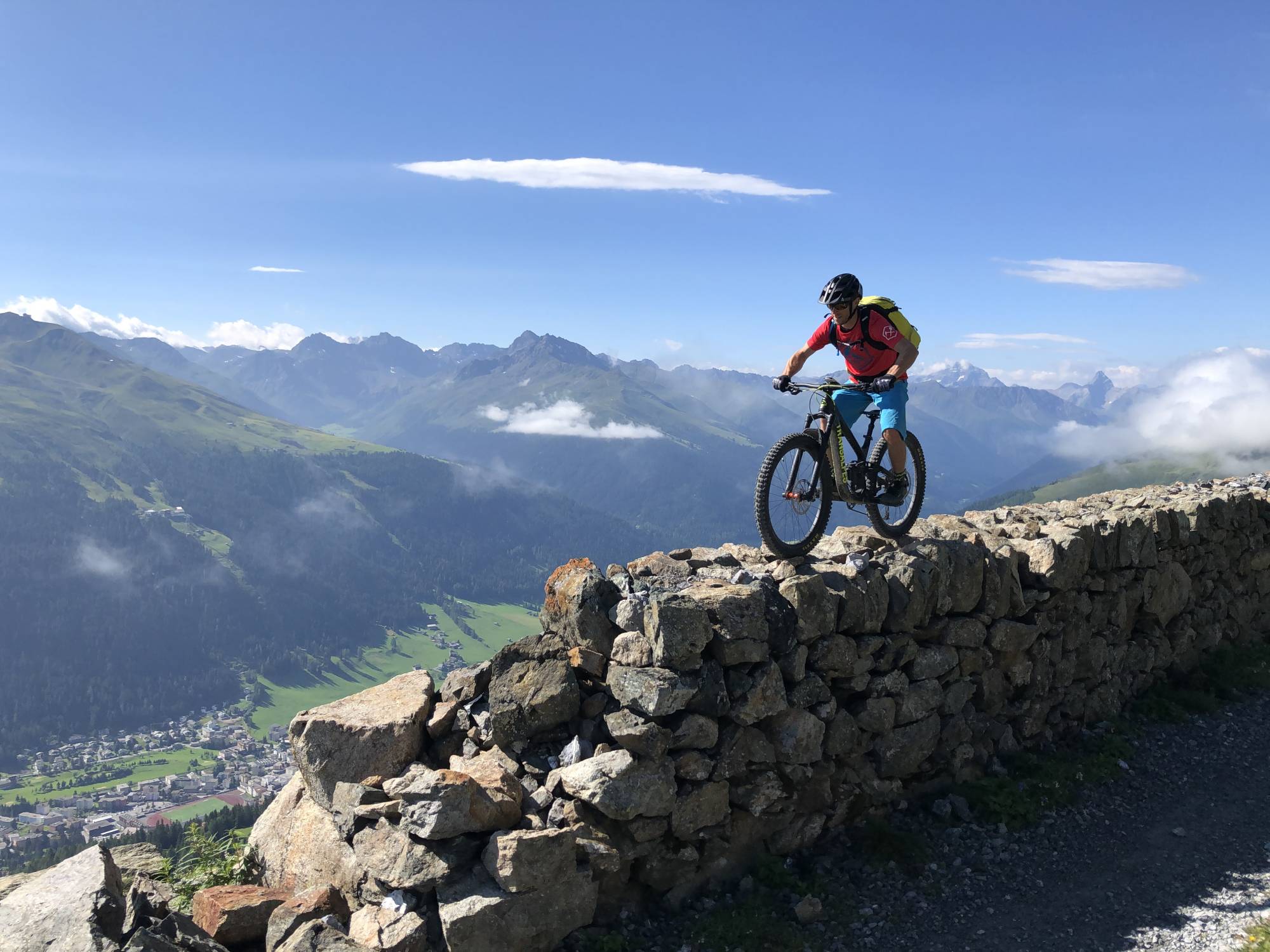 Mountainbike-kurs i körriktning med en cyklist på en klippa. Omgivning: Alperna, klar himmel, frisk luft.