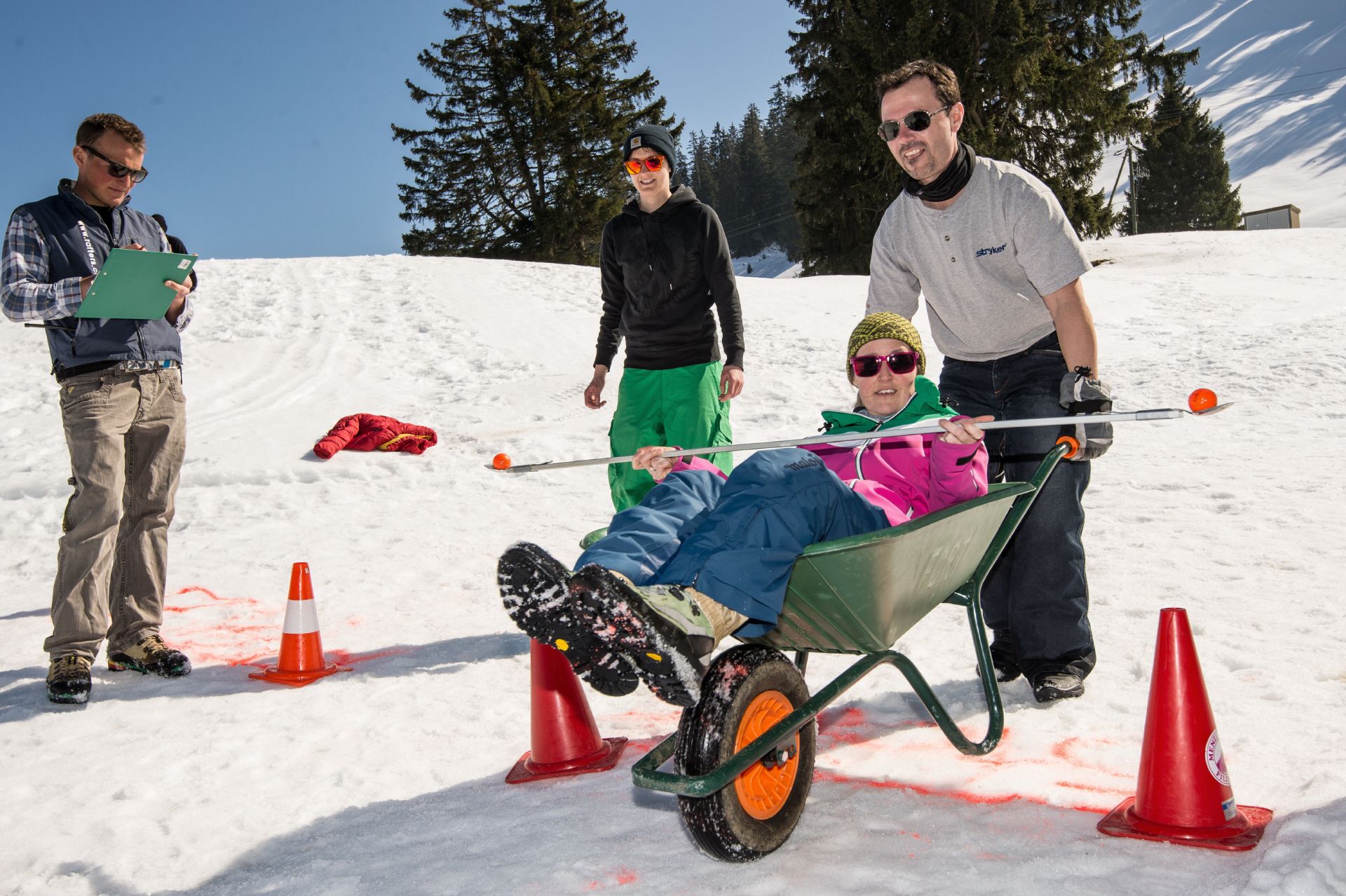 Ομαδικό γεγονός Χειμερινών Ολυμπιακών Αγώνων στην Ελβετία, συμμετέχοντες με καρότσι στο χιόνι, χαρούμενη ατμόσφαιρα.