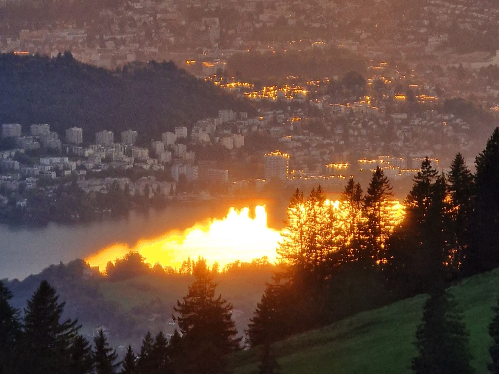 Seebodenalp: Wunderschöner Sonnenuntergang über dem See und der Stadt, umgeben von Wäldern.