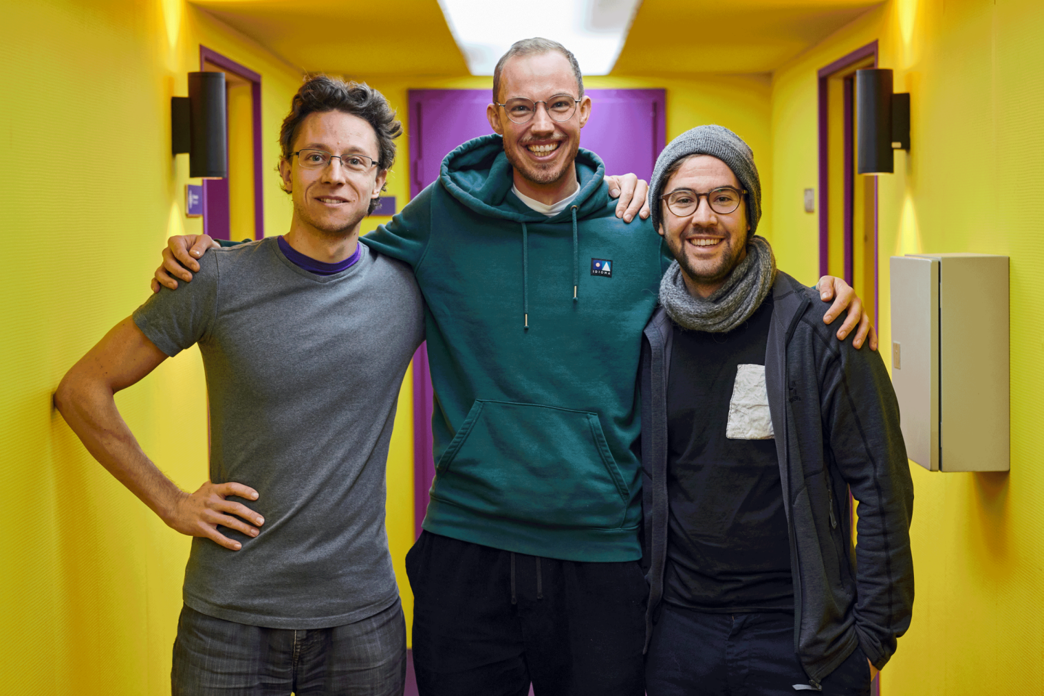 Amis : trois hommes rient dans un couloir lumineux, idéal pour le teambuilding et les activités de groupe