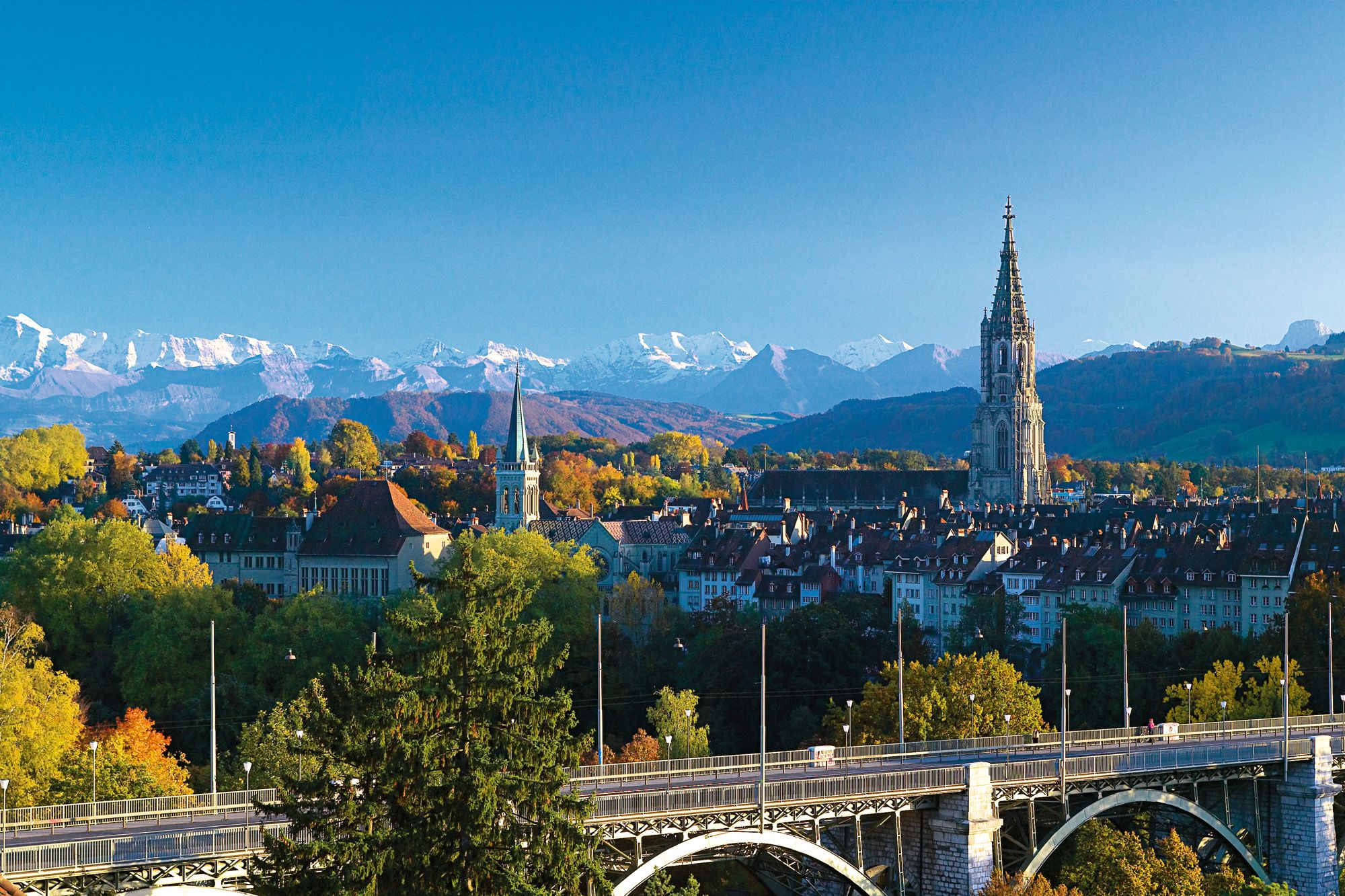 Bern: Uitzicht op de hoofdstad met een brug, bergen en huizen op de achtergrond.