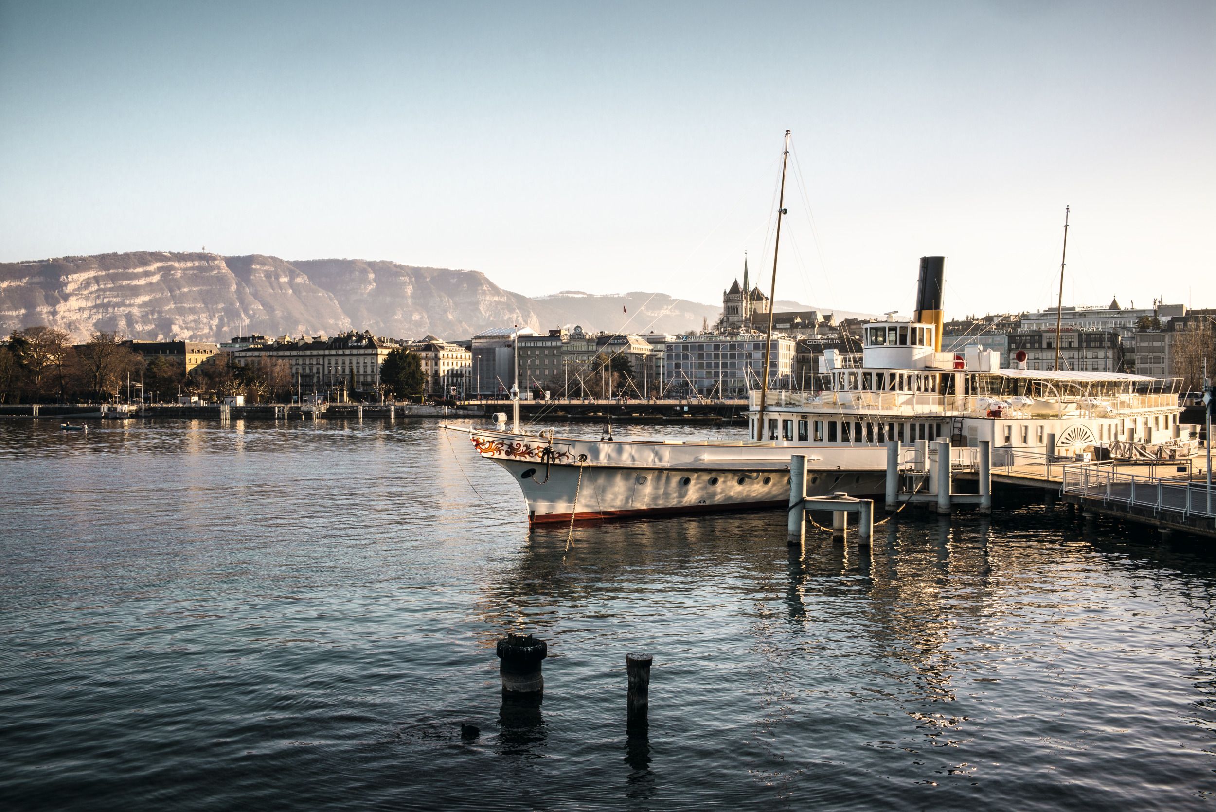 Navio no porto de Genebra com vista para a cidade e as montanhas, ideal para relaxamento e exploração.