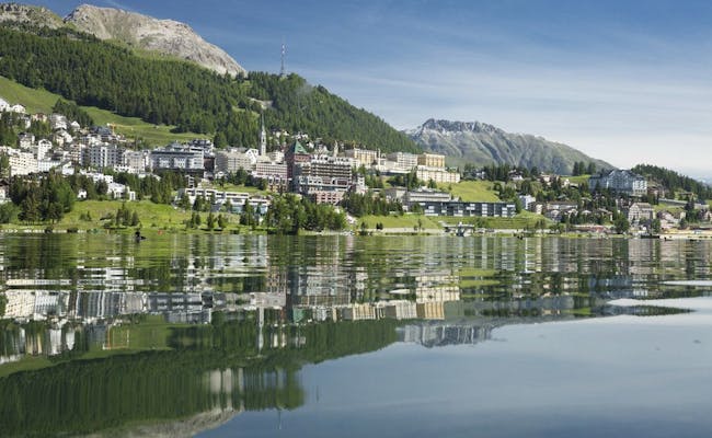 St. Moritz by med vattenspegling, tydlig bergsbakgrund, blå himmel.