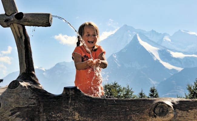Drikkevand ved brønden: Børn nyder naturen i Schweiz om sommeren.