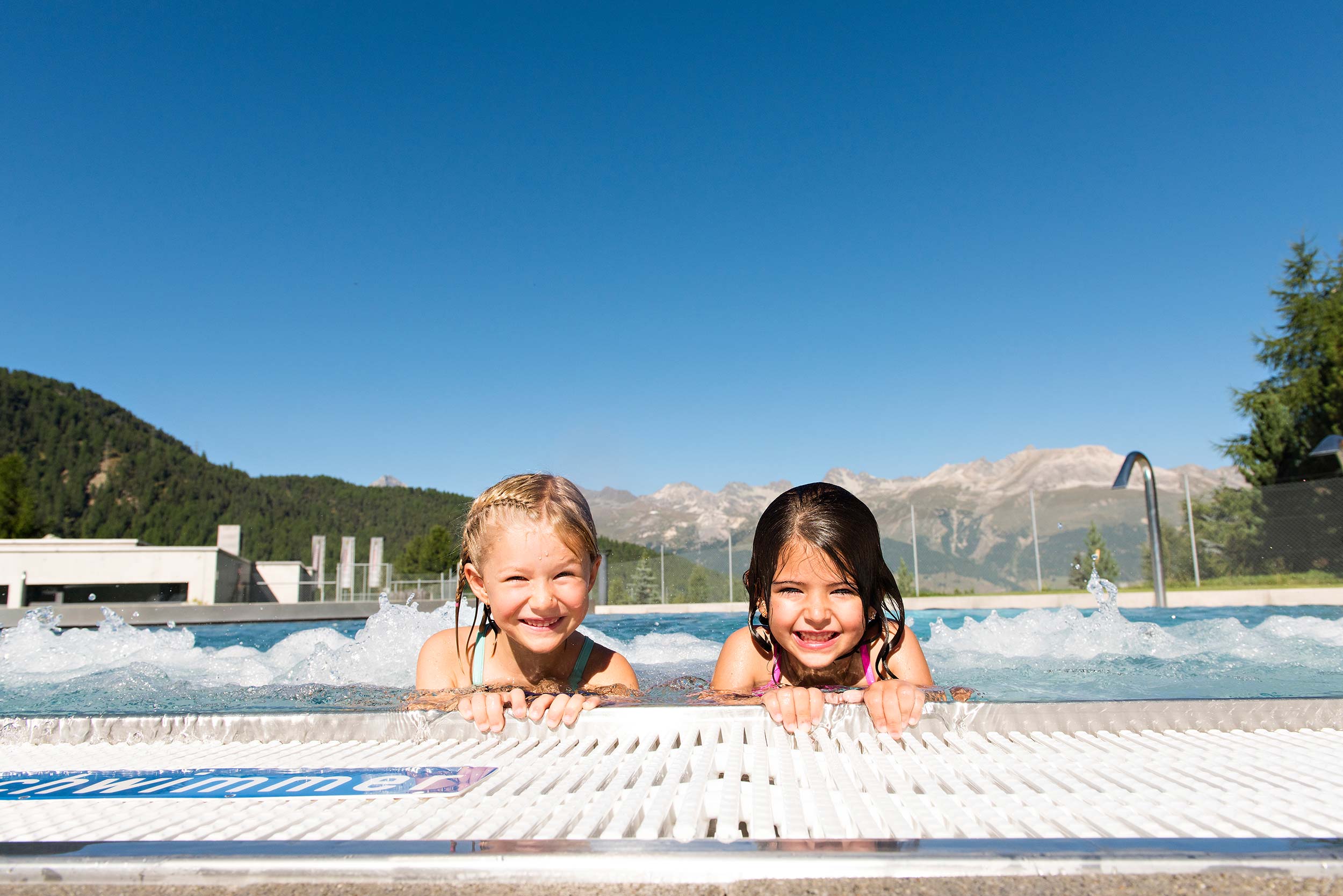 Children enjoy swimming in the water park Bellavita during summer with a view of the mountains.