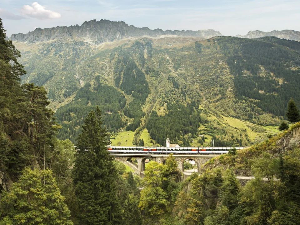 تجاوز Gotthard Panorama Express الجسر في واسن، في جبال خضراء.