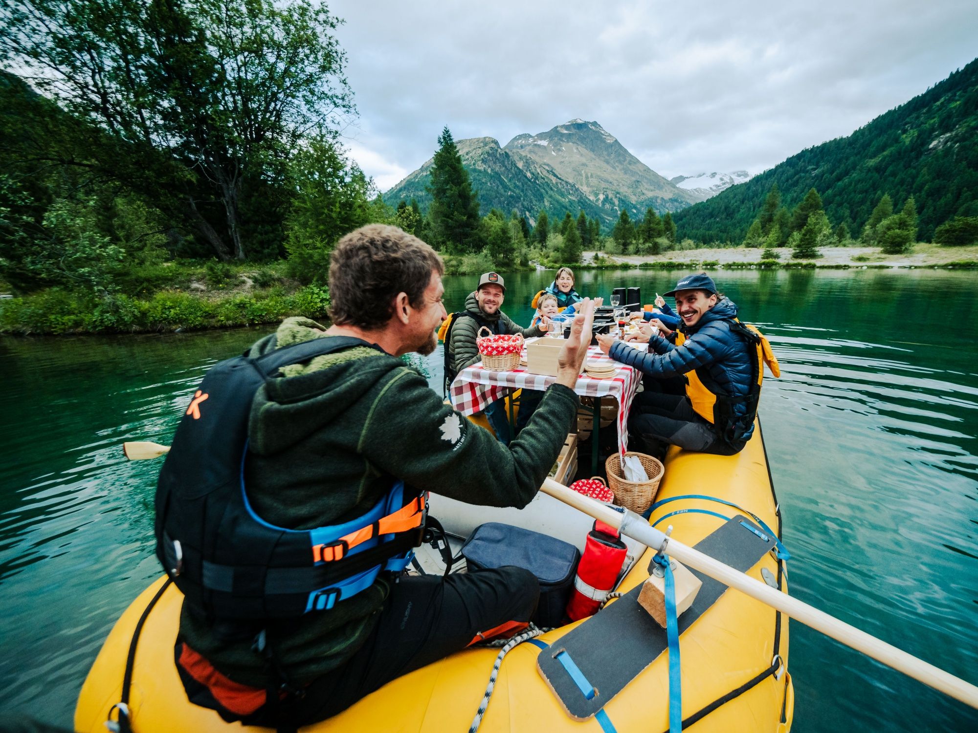 Raclette picnic by the lake with friends, surrounded by mountains and natural landscape.