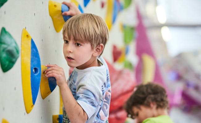 Ragazzo che scala nel parco divertimenti indoor con prese di arrampicata colorate