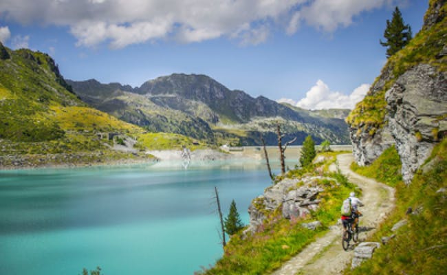 Mountainbike MTB 4 Seentour em um caminho de cascalho ao longo do lago, cercado por montanhas e verde