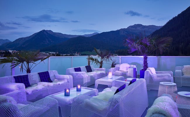 Davos Hotel Hard Rock mit Lounge-Möbeln, Palmen und Bergen im Hintergrund