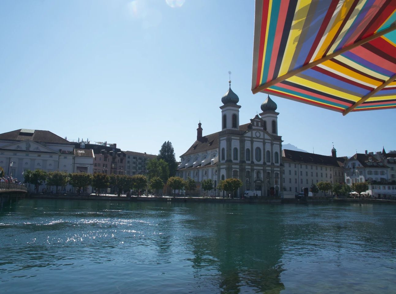 Iglesia jesuita en Lucerna con vista al agua y paraguas colorido, ideal para relajación y aventura.