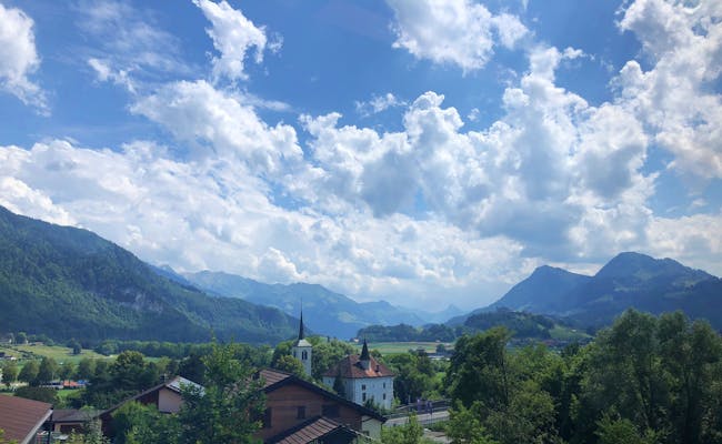 Paesaggio di Gruyères con montagne e chiesa sotto un cielo azzurro.