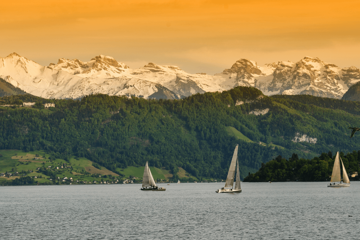 Sunset cruise with champagne on a lake in Switzerland, sailing boats and mountains in the background.