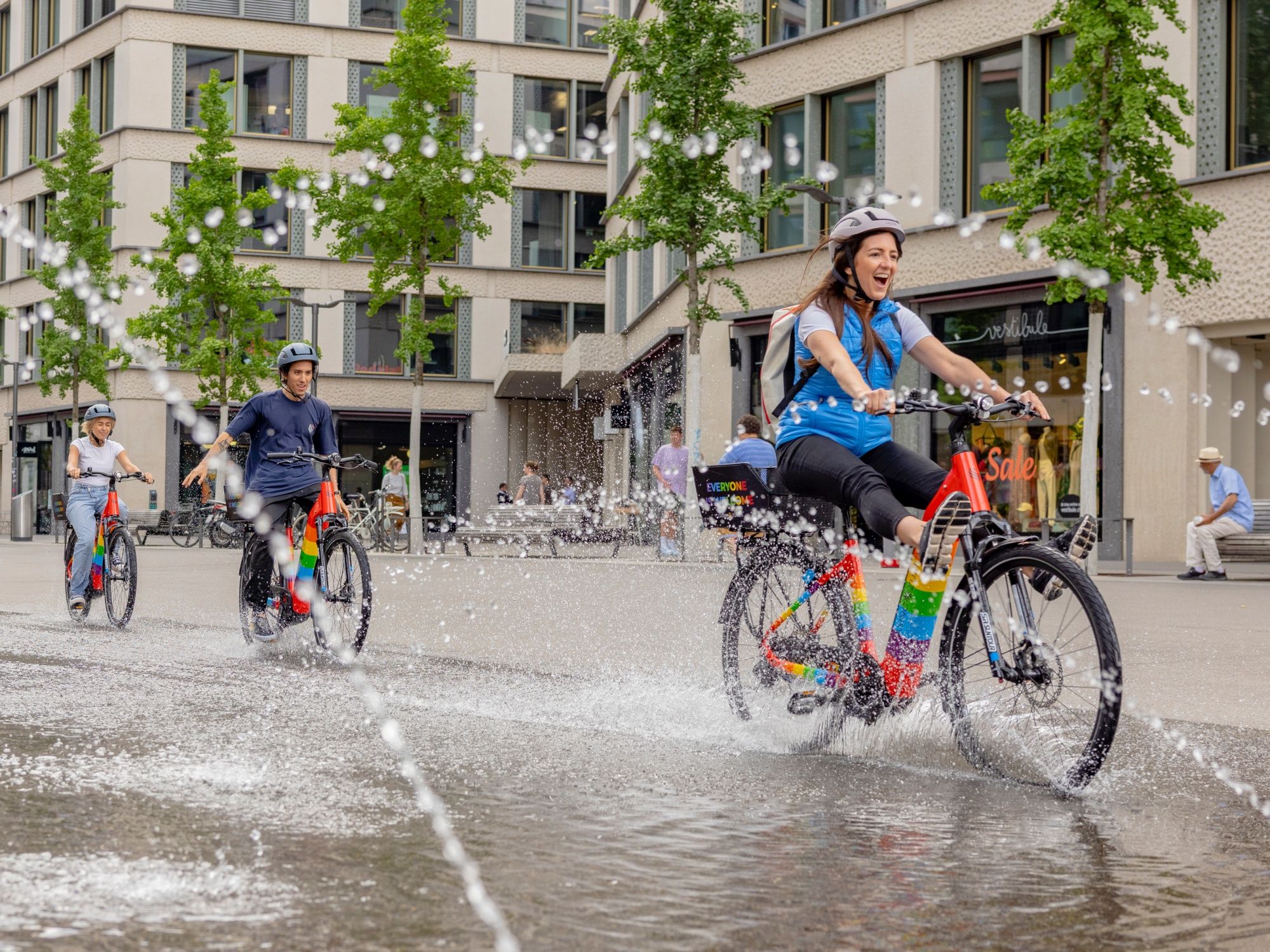 E-Bike Tour in Zürich mit fröhlichen Radfahrern und spritzigem Wasser am Straßenrand.