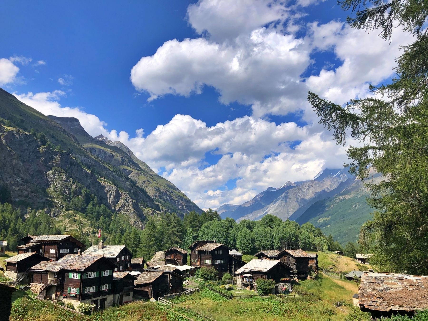 Zermatt: Hikers explore the alpine landscape with traditional chalets and green meadows.