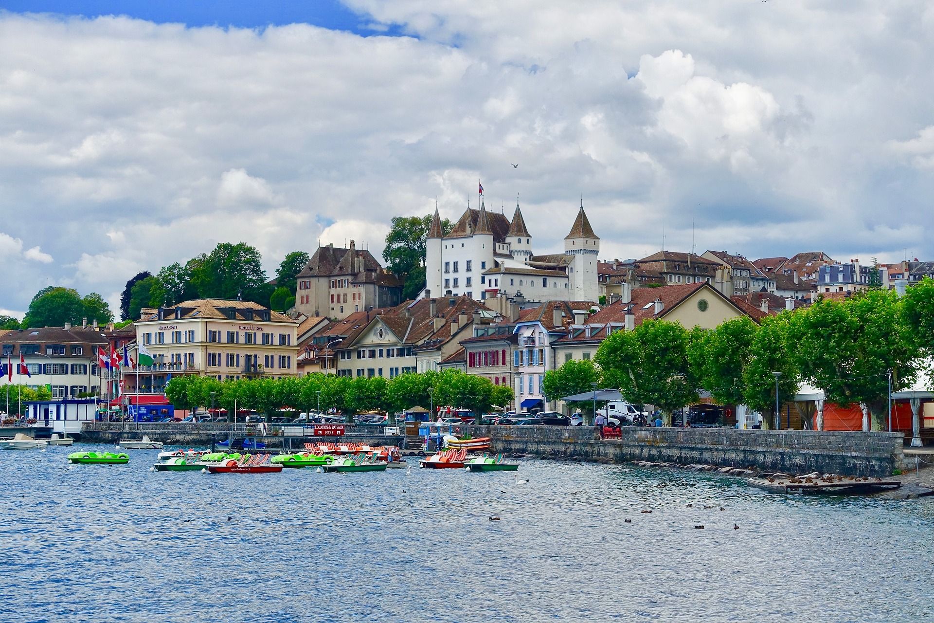 Port of Nyon with colorful boats, picturesque city view, and clear water.