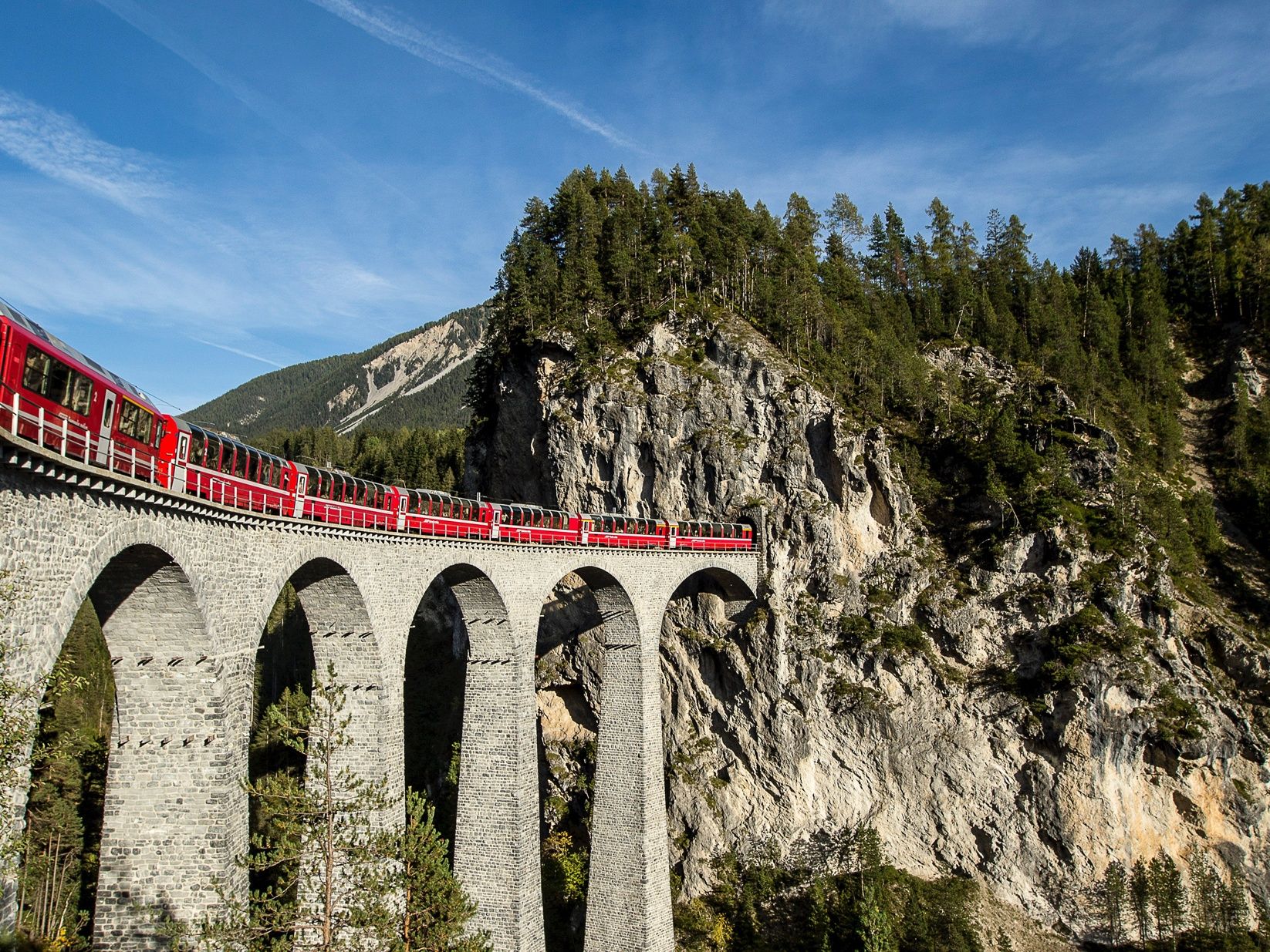 Landwasser Viaduct crosses a gorge with a red train in the Swiss Alps.