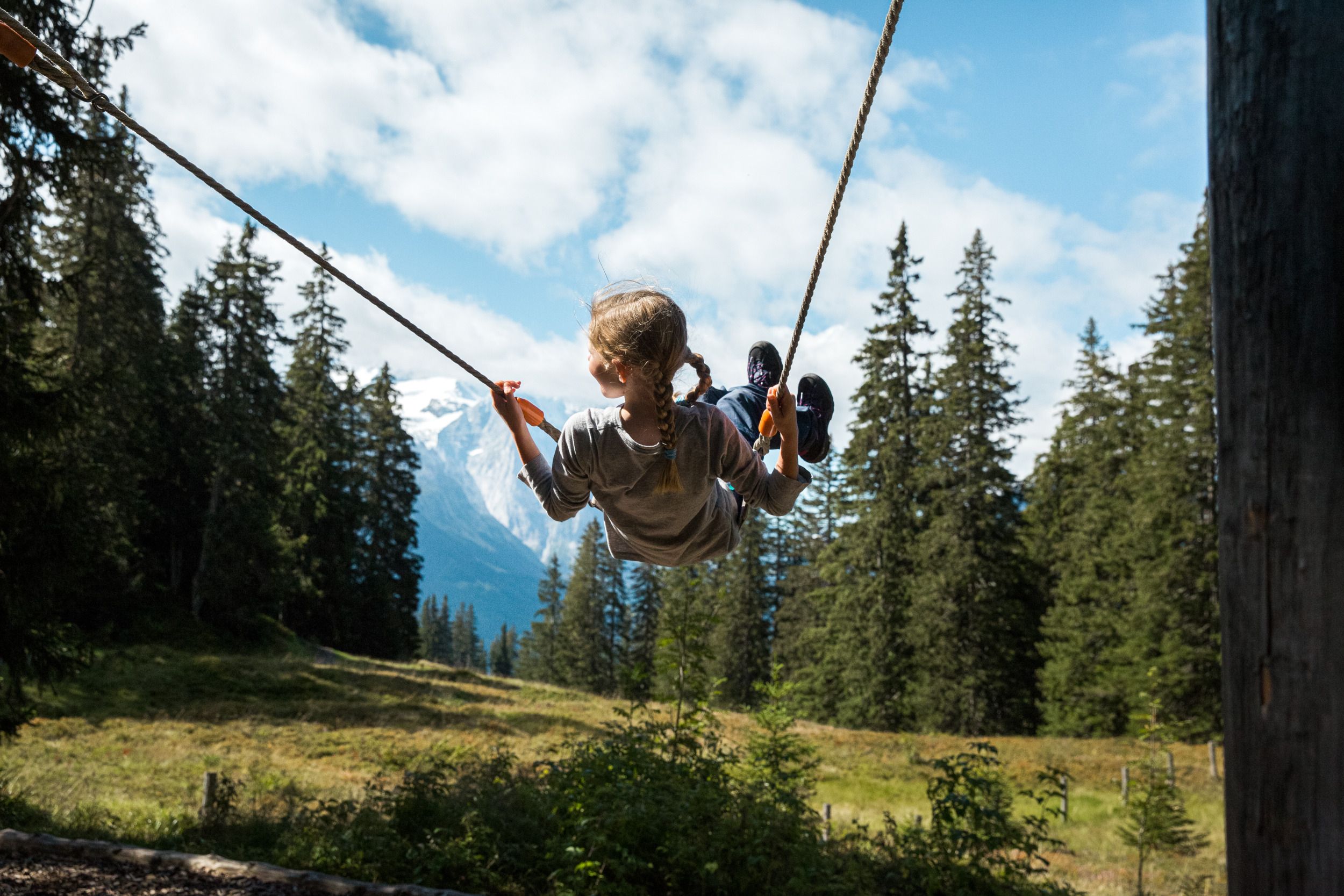 Dítě houpe, výhled na les a hory, okolí s stromy, jasná obloha
