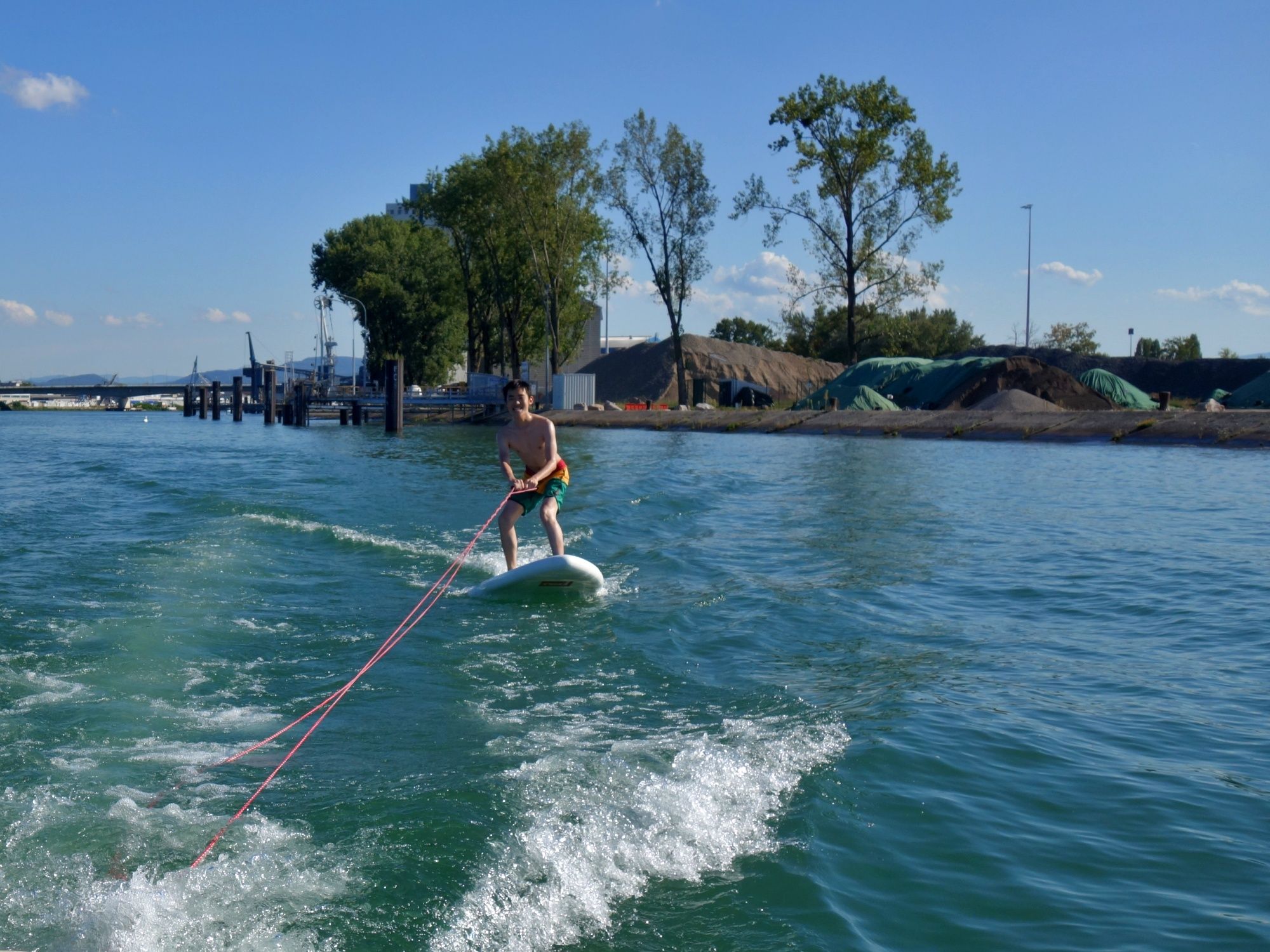 Pelayaran Bot: Seorang budak lelaki meluncur di atas air di bawah panas matahari dengan pelbagai pokok di latar belakang.