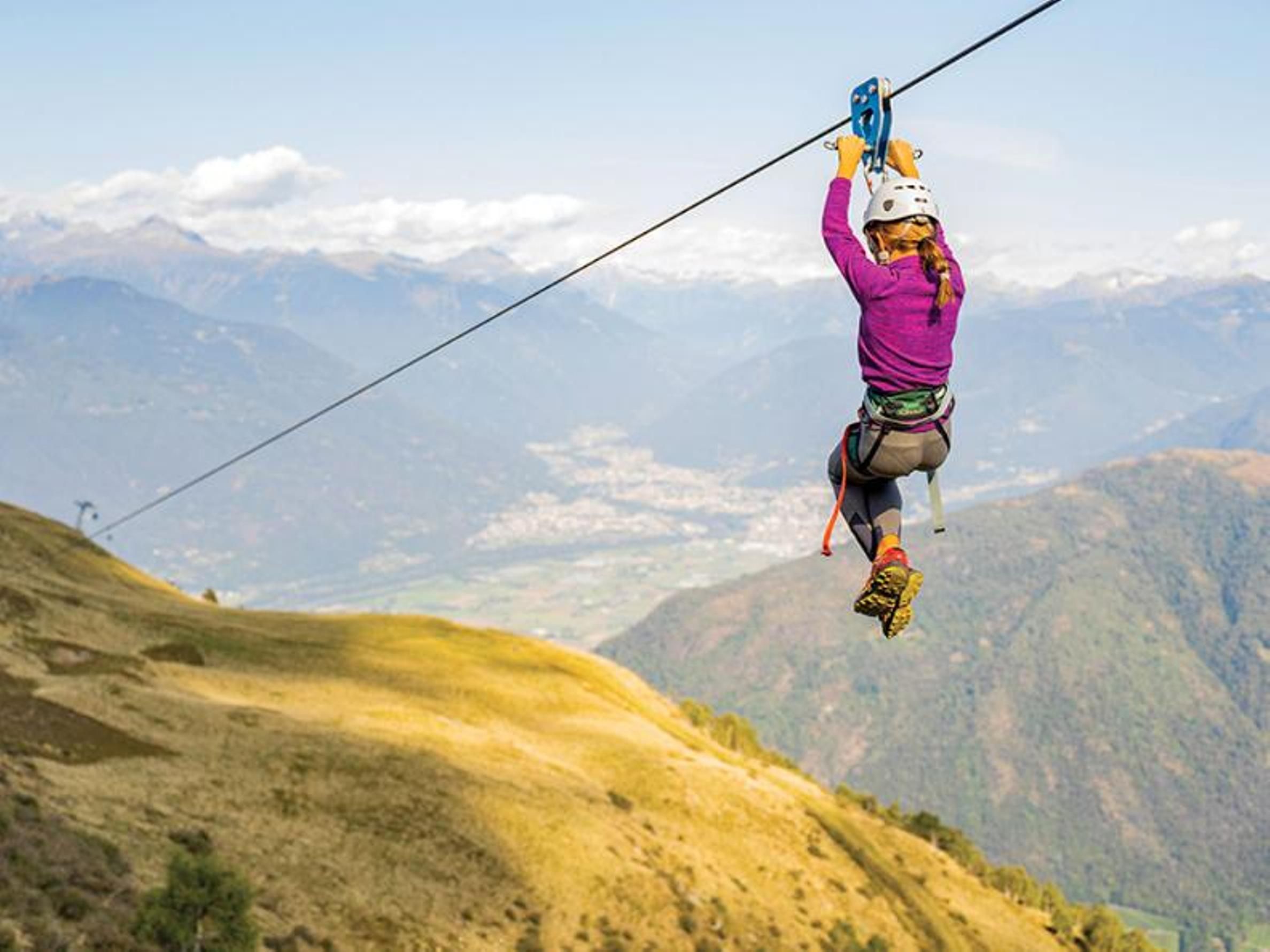 塔马罗山的滑索，俯瞰美丽的景色。一个穿着紫色衣服的人在绳索上悬挂，穿越山间景观。