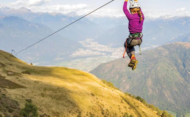 Tiroliña en el Monte Tamaro con vista al paisaje. Una persona vestida de morado flota sobre la cordillera mediante un cable.