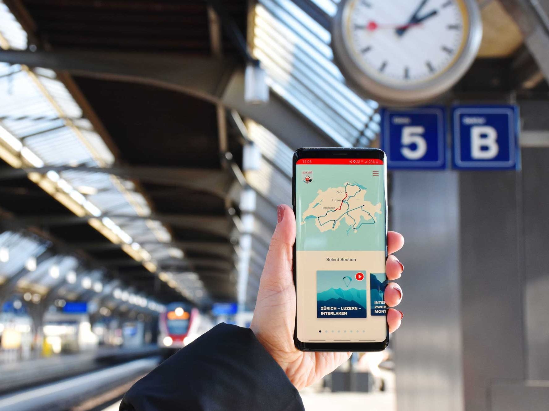 الهاتف يُظهر خريطة السفر في سويسرا عند المحطة. رصيف القطار وأعمدة الانتظار مرئية.