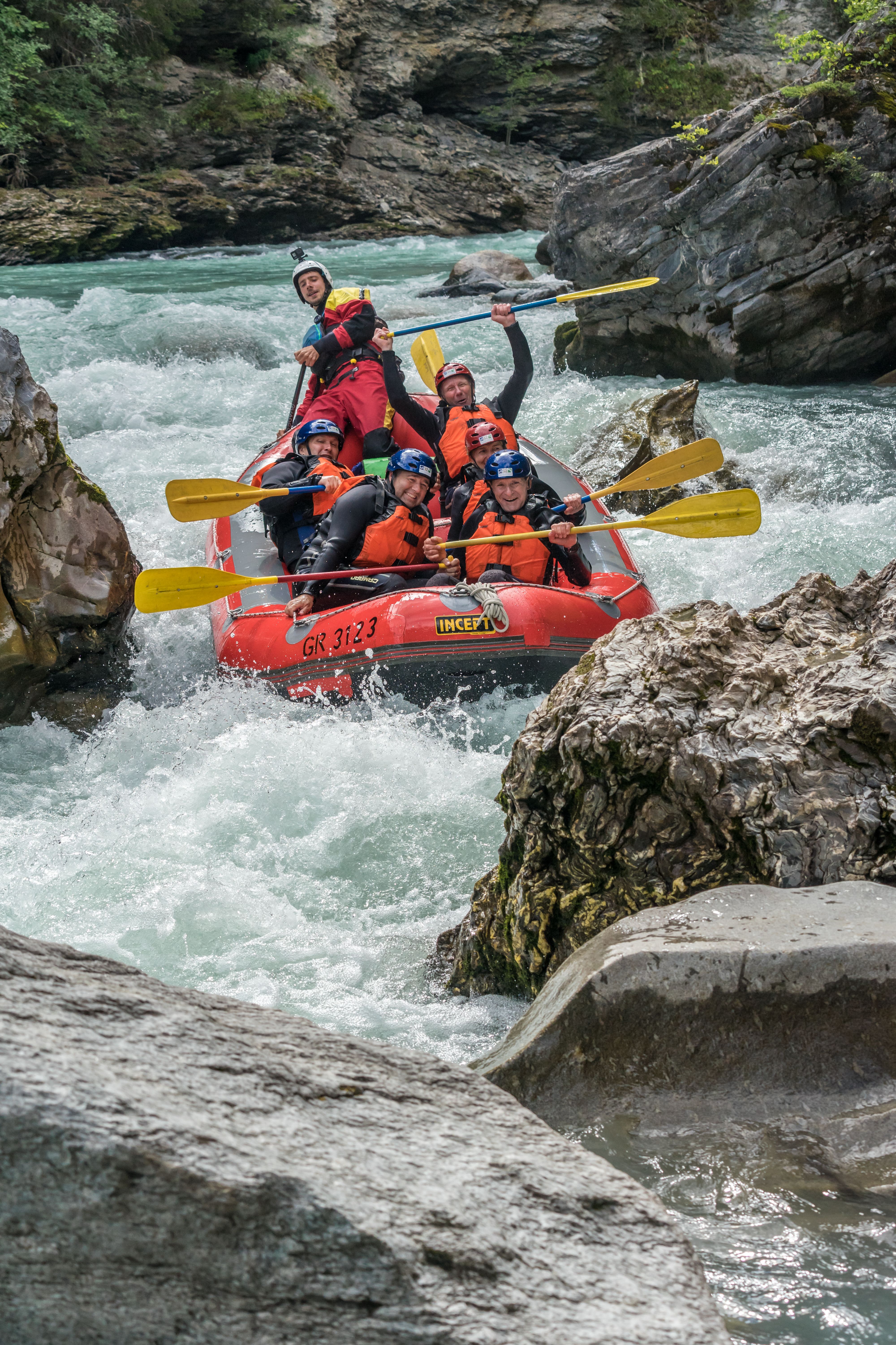مغامرة التجديف في المياه المضطربة على نهر جيارسون في إنغادين. المشاركون في سترات برتقالية يجدفون. الجبال في الخلفية.