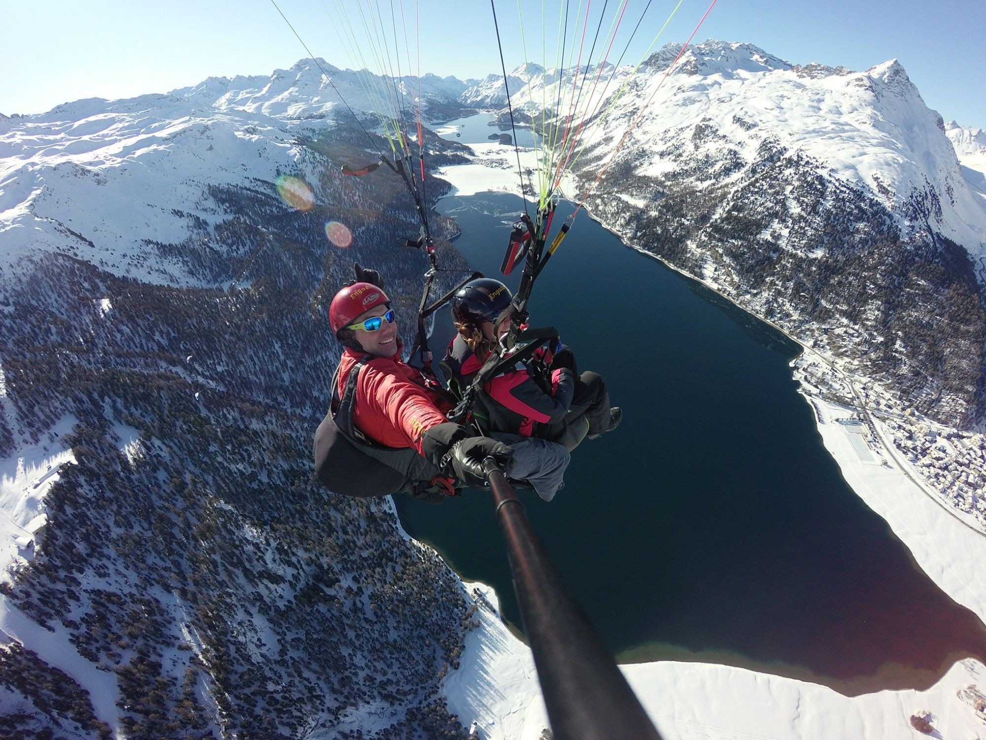 Gleitschirmfliegen im Engadin: Winter Tandemfliegen über schneebedeckte Berge und einen glitzernden See.