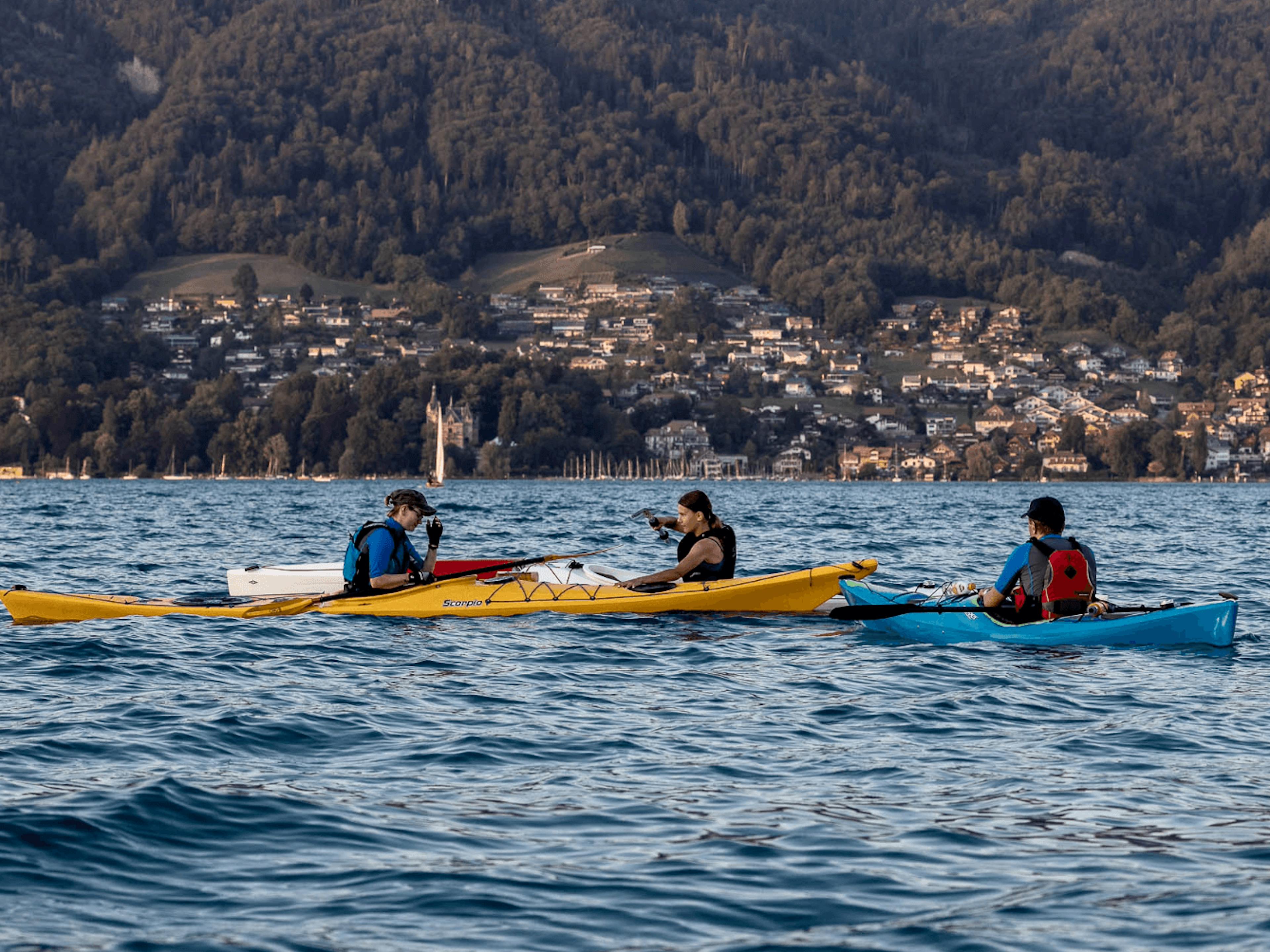 Kajak mieten: mehrere Kajaks auf dem Thunersee mit Blick auf die umliegenden Berge und Dörfer.