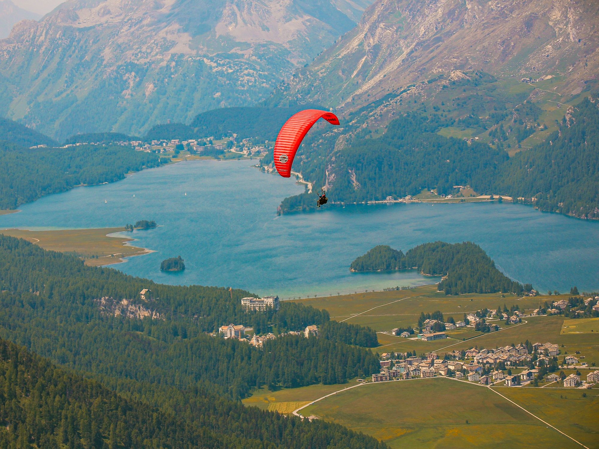 Samedan Tandemflug: Paragliding über dem Engadin mit Blick auf den See und die Berge.