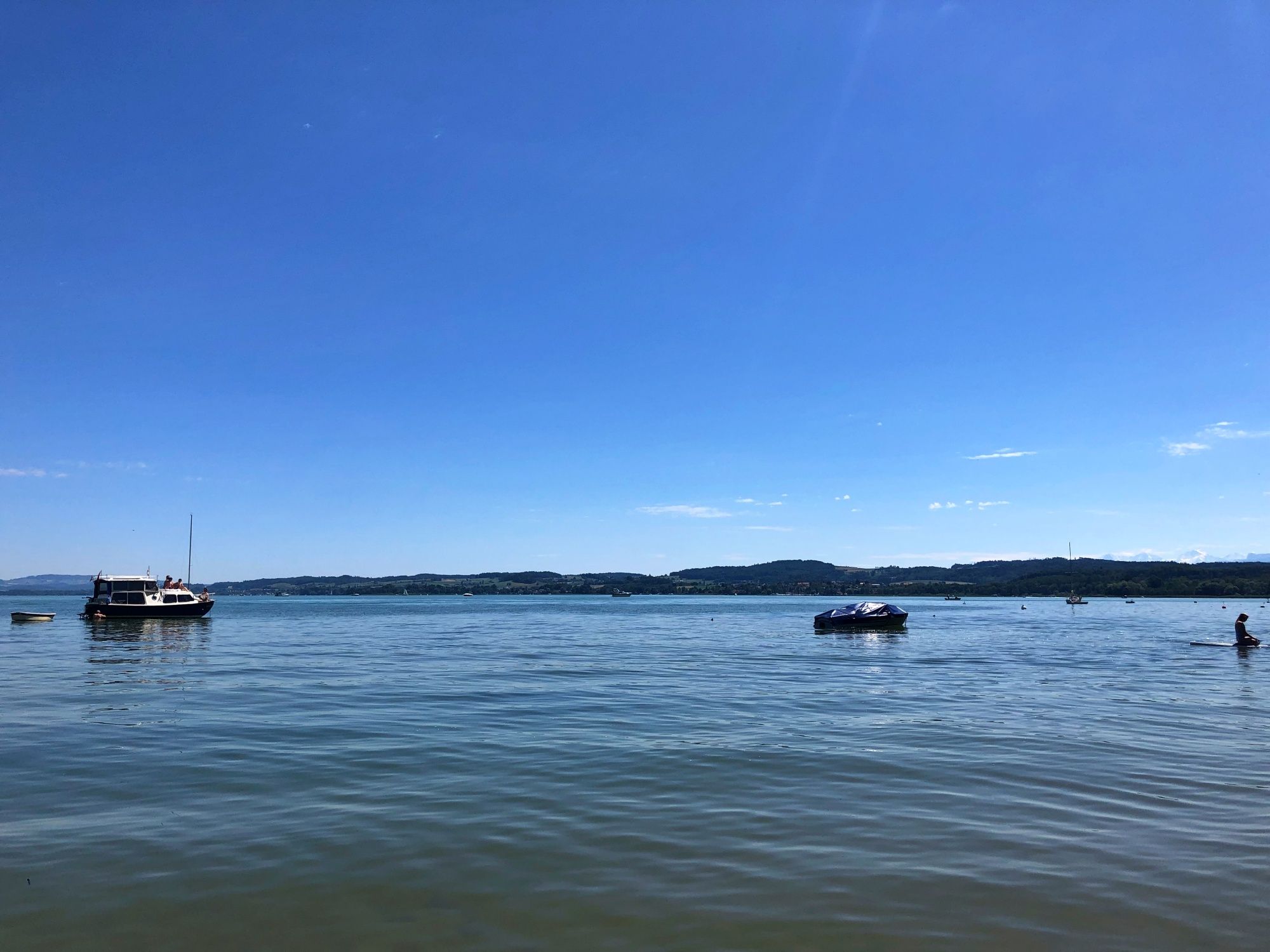 Pláž Salavaux u jezera Murten s loděmi a vodními sporty v létě.