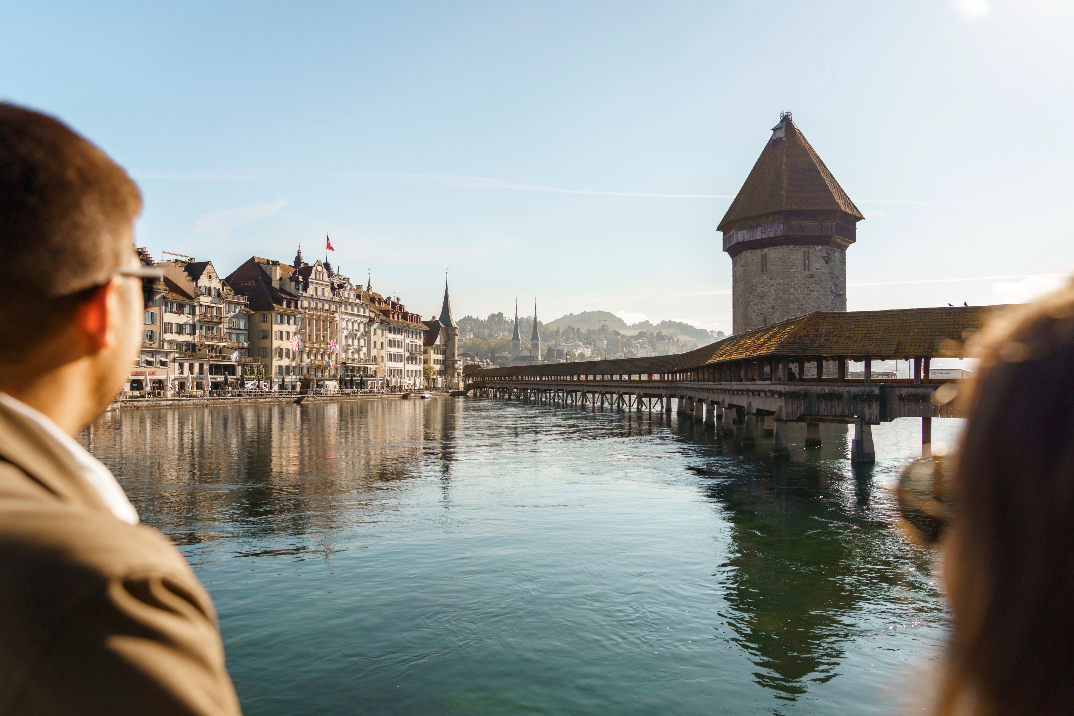Lucerne: View of the Chapel Bridge and historical buildings by the water under a clear sky.
