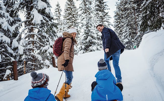 Familia deslizándose en la nieve, entorno forestal, clima invernal