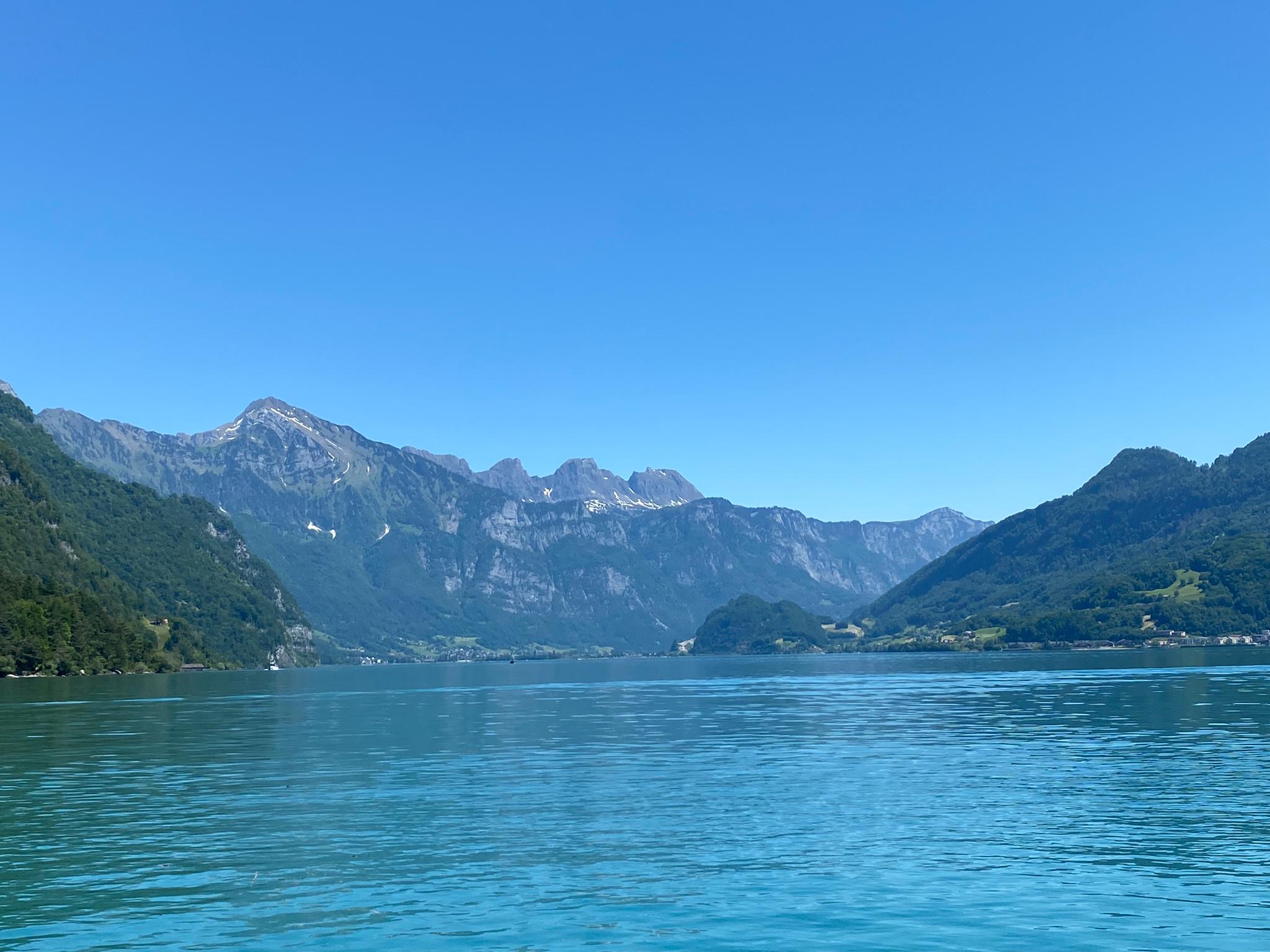 Lacul Walensee cu apă limpede albastră, înconjurat de munți sub un cer senin albastru