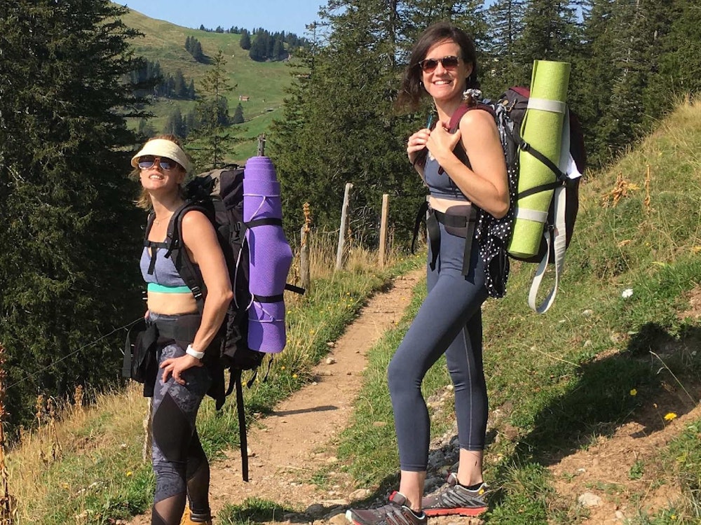 Yoga Rigi Kulm mit zwei Frauen beim Wandern, ausgestattet mit Matten und Rucksäcken auf einem Wanderweg.