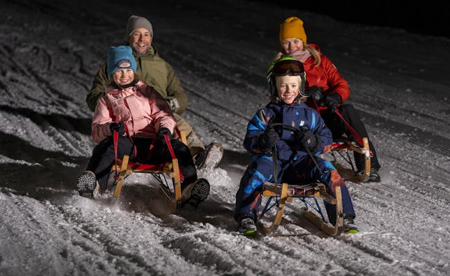 Νυχτερινή παιδική χιονοδρομία στο Flims Laax με οικογένειες σε σκι στο σκοτάδι.