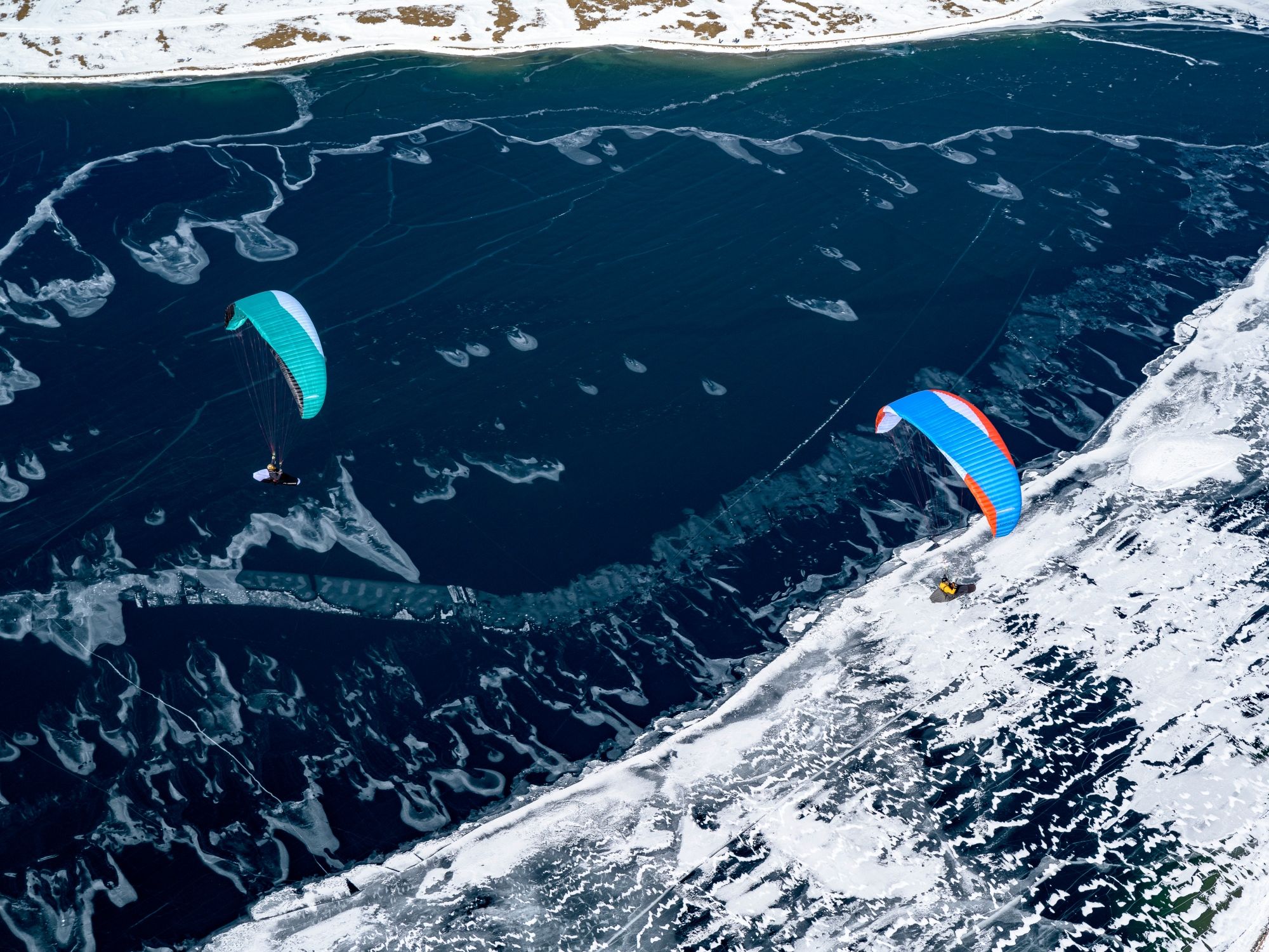 Paragliding i Engadin med piloter over glitrende vand og sneklædte bjergtoppe.