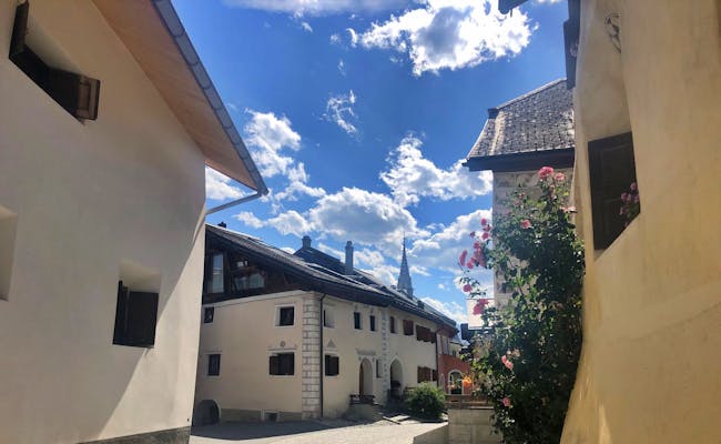 Engadin: Typische Dorfhäuser in einer Gasse des Engadins mit blauer Himmel und Blumen.