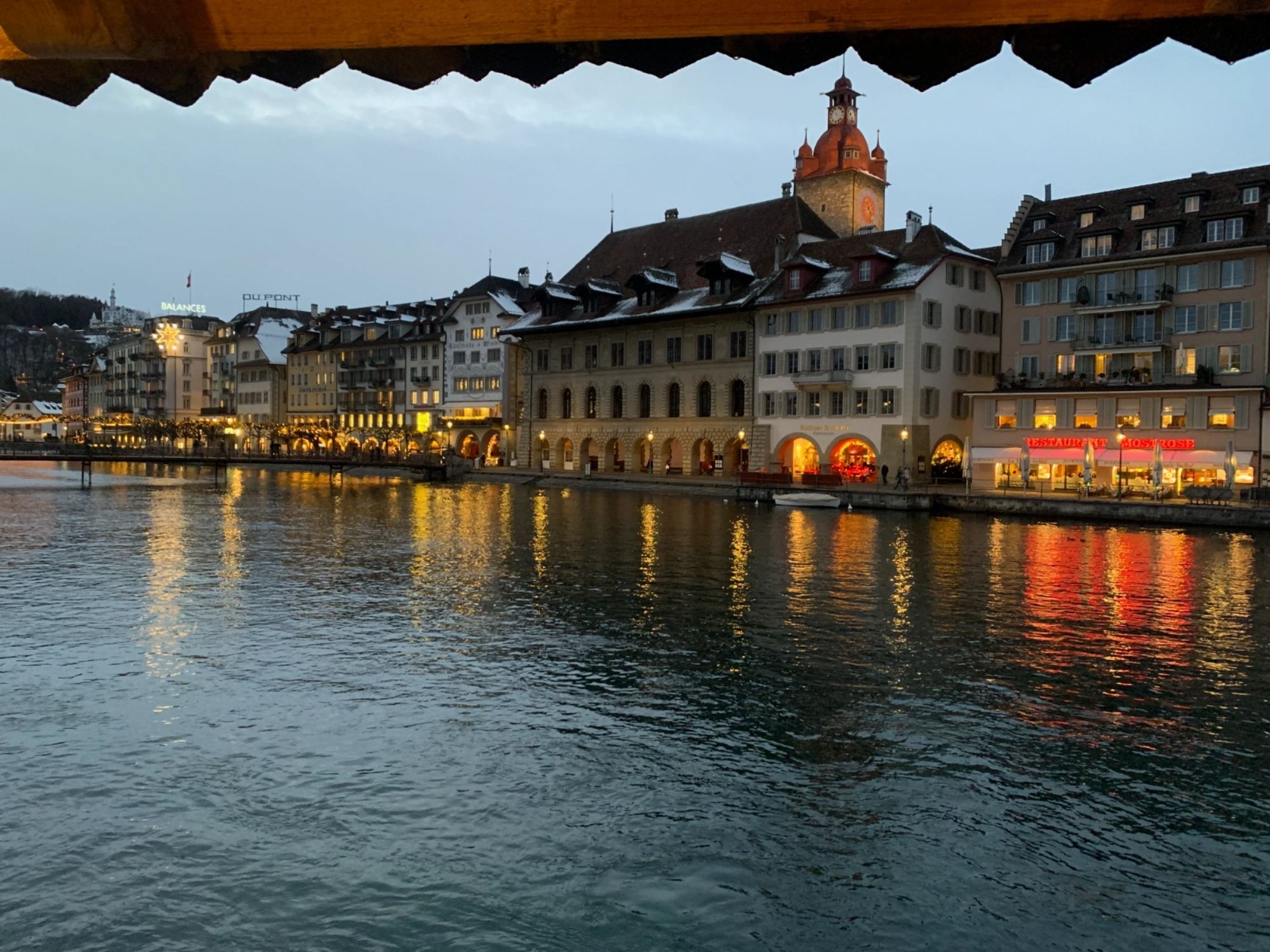 लुज़र्न: पानी के किनारे रात्रि में रोशनी से जगमगाते भवन के साथ शहर का दृश्य। सर्दियों में रोमांटिक माहौल।