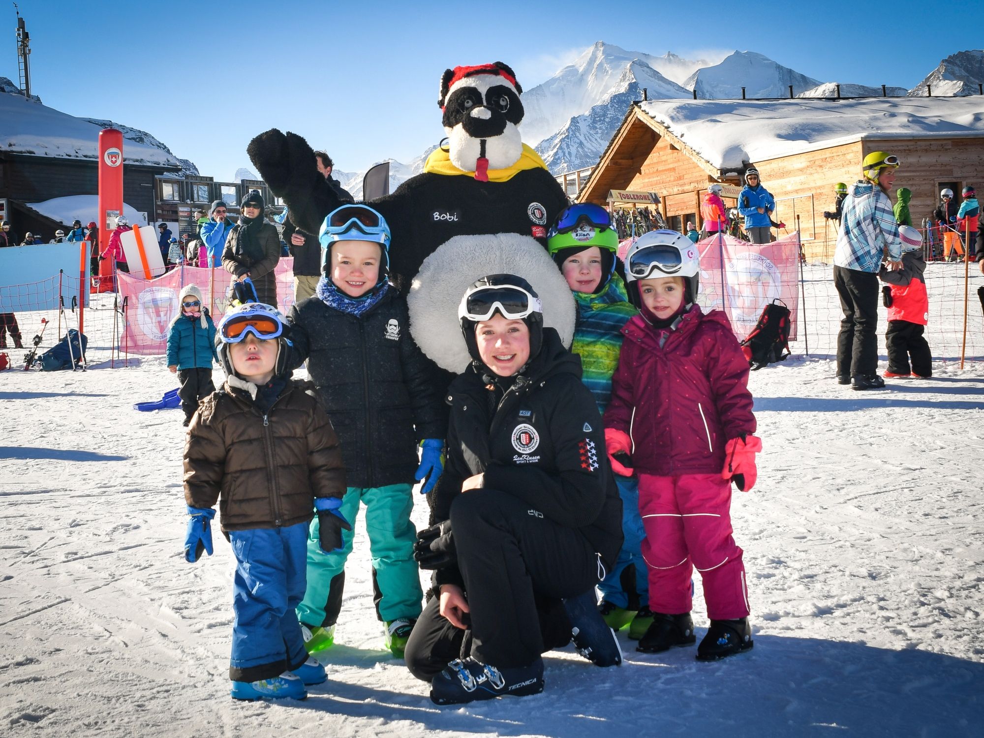 Skischool Hannigalp: Kinderen in de skikindergarten met skileraren in de sneeuw, winteractiviteit.
