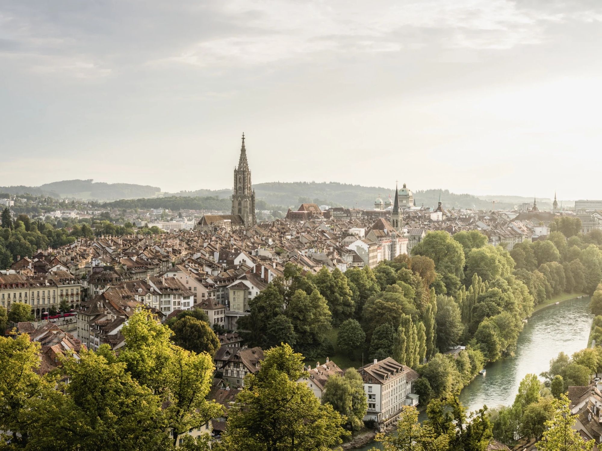 Výhled na Bern s pohledem na staré město a řeku Aare, obklopený stromy.