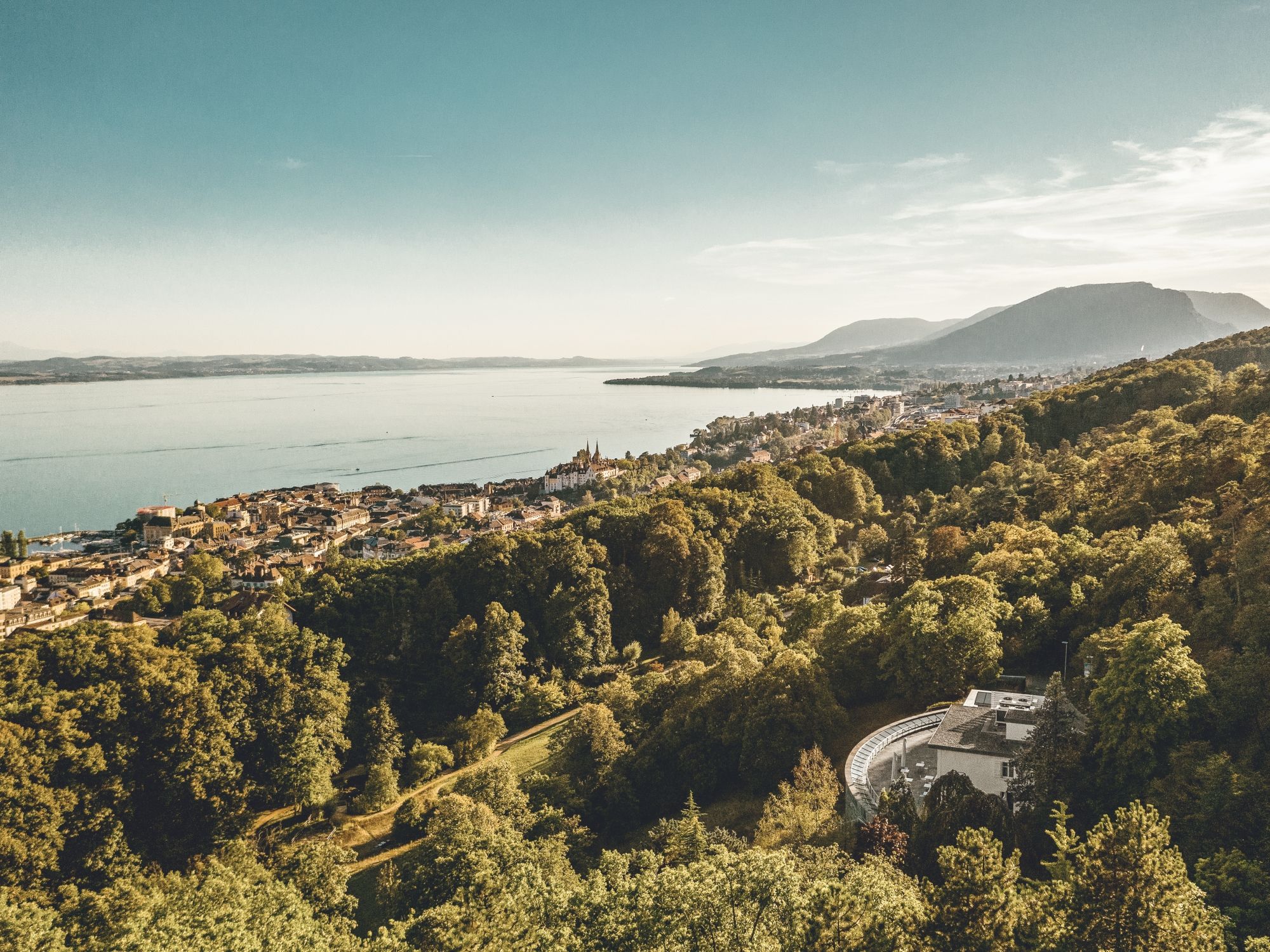 Lago di Neuchâtel con un paesaggio costiero pittoresco, circondato da boschi e montagne.