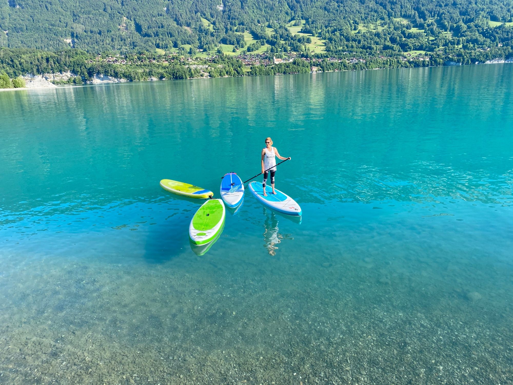 SUP na jezeře Brienz s průzračnou vodou a zelenou horskou krajinou v pozadí.
